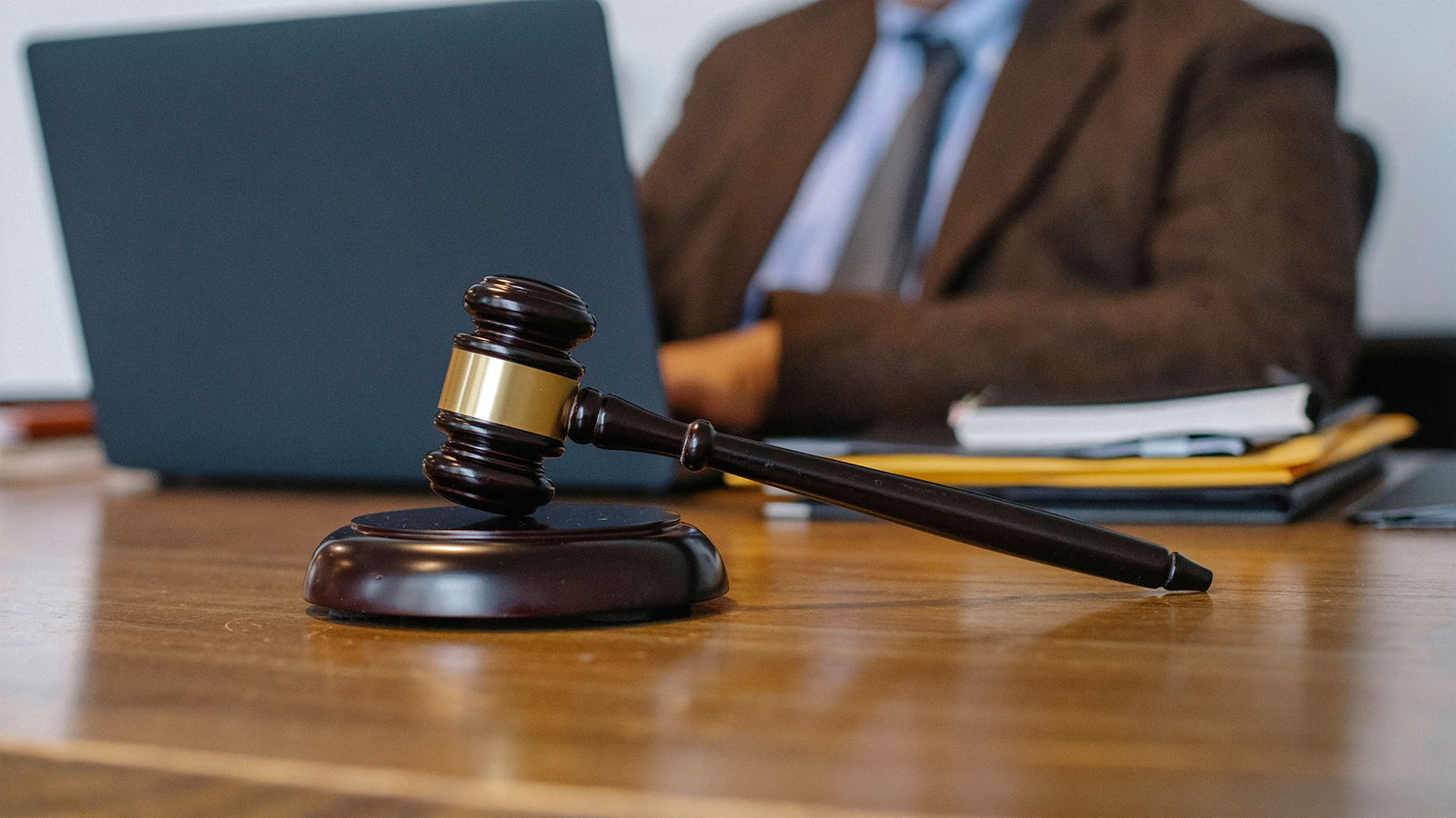 A lawyer in a formal setting working on a laptop with a gavel in focus on the desk.